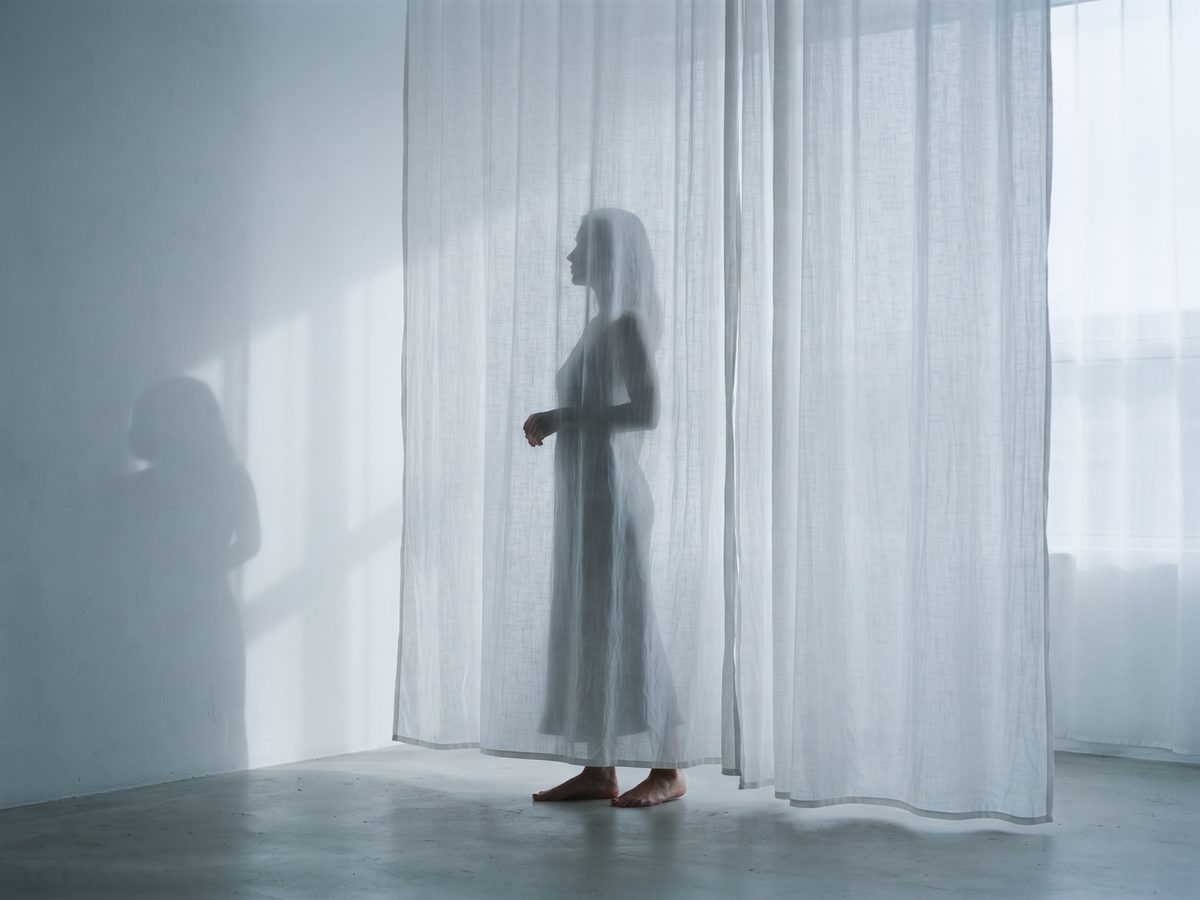Silhouette einer Person hinter einem durchscheinenden Vorhang, Schatten an der Wand