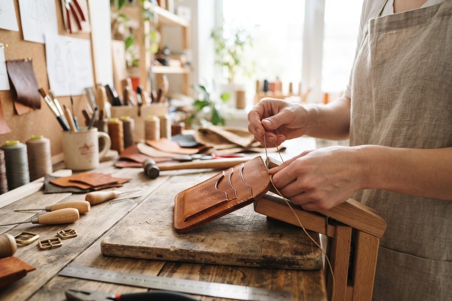 Hände bei der Lederarbeit an einer Werkbank im hellen Atelier