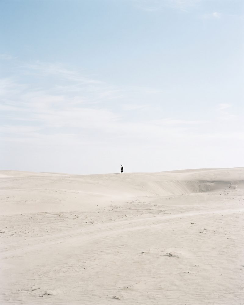 Winzige Figur in einer weiten, hellen Dünenlandschaft