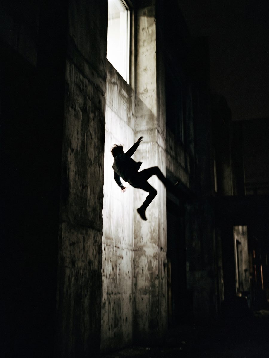 Dunkle Figur im Sprung in einem Lichtschacht aus rohem Beton